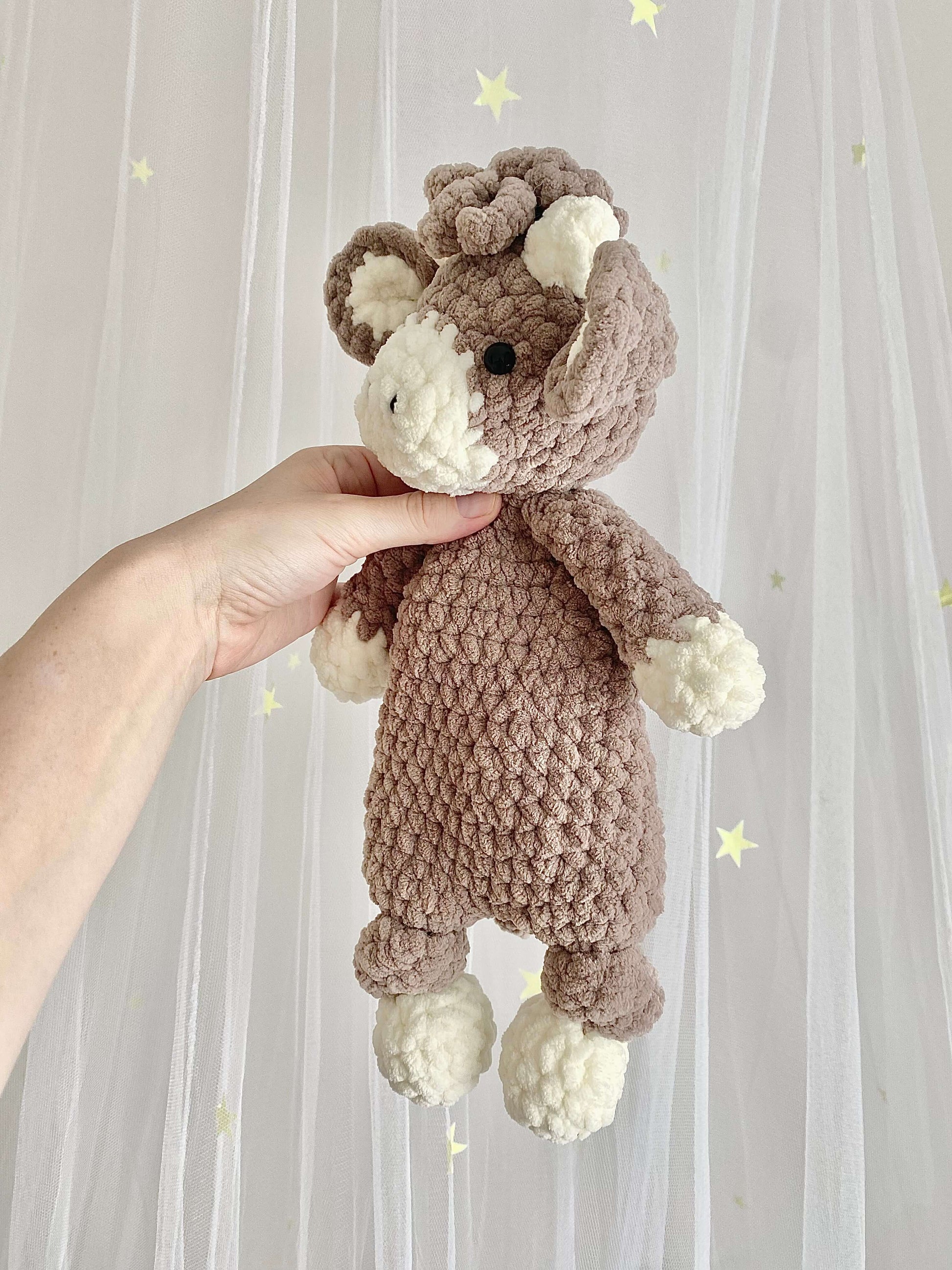 A Highland Cow amigurumi plushie designed as a crochet pattern using super bulky chenille yarn. The plush snuggler features detailed stitching, textured fluffy fur, and a comforting, soft feel for children.